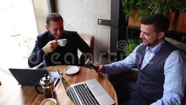 两个商人坐在咖啡桌上，用手提电脑，<strong>喝茶</strong>，<strong>聊天</strong>